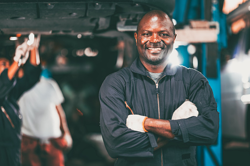 portrait garage mechanic professional worker car engine service looking camera smile arm crossed