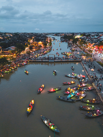 drone view on illuminated boats floating on river in Hoian old town, people walking at river promenade