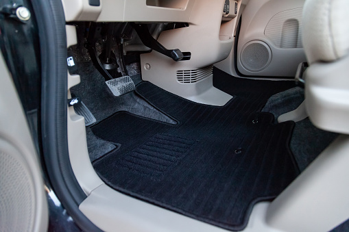 Clean car floor mats of black carpet under front driver seat in the workshop for the detailing vehicle before dry cleaning. Auto service industry. Interior of sedan.