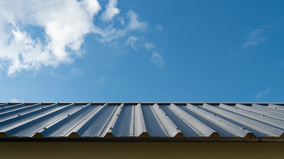 Blue roof metal sheet arranged on the roof. Hip Roof of the house is beautifully lined. Construction of a house under the blue sky and white clouds.