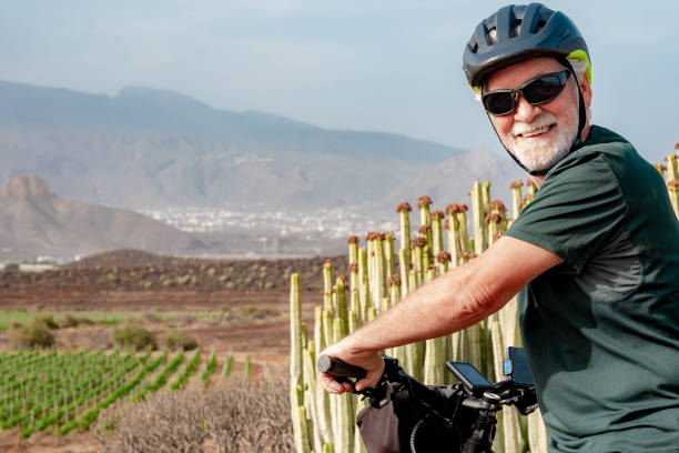 happy cyclist senior man with protective helmet riding bicycle in the countryside on a sunny day. handsome bearded male enjoying healthy lifestyle and sport activity - senior adult human face male action imagens e fotografias de stock