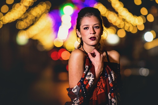 A Caucasian woman posing with the blurred bokeh city lights at night
