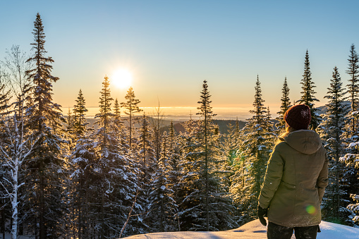 Portrait of a woman relaxing on a snowcapped mountain during a sunrise of winter near Lac-Beauport in Quebec.