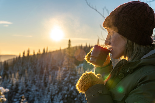 Portrait of a woman having a coffee and relaxing on a snowcapped mountain during a sunrise of winter near Lac-Beauport in Quebec.