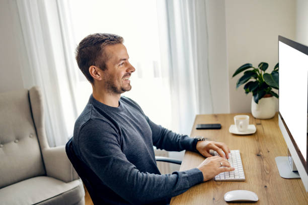 istock A young man is working from his home office remotely, typing on a keyboard and smiling at the monitor. 1449845269