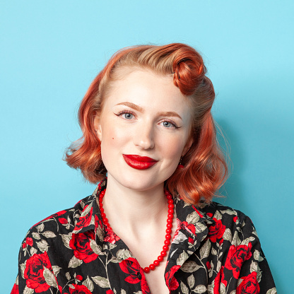Studio portrait of a cheerful red-haired white woman in a bright blouse and red beads against a blue background