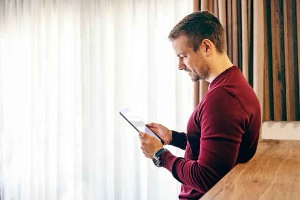 istock Profile of a happy man reading newspaper on the tablet while leaning on kitchen counter. 1449846107