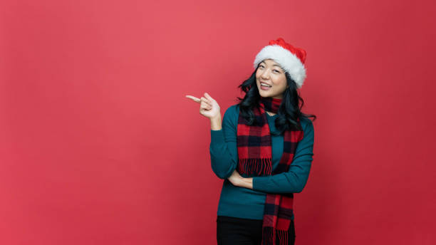 istock Christmas sale concept. Happy young woman pointing at empty space on red studio background, panorama. Pretty lady in Santa hat and warm sweater making Xmas promotion or special offer 1449850165