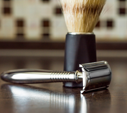 shaving brush and t-shaped metal razor on a wooden table in the bathroom