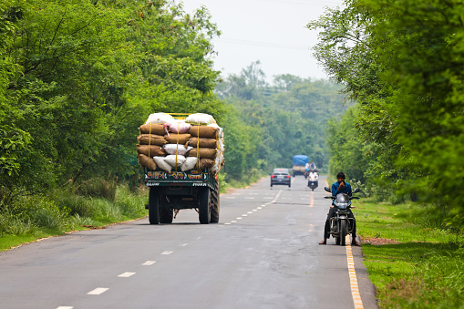 May 31, 2021 - Katwa WB India : Picture of countryside highway in state of West Bengal in India. The two lane highway running straight and peoples are using motorcycle and other vehicle plying on it. The road running through the forest and covered by thick canopy.