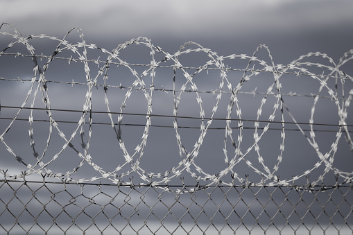 Fince with a roll of barbed wire on top as part of a state border with dark clouds in the background