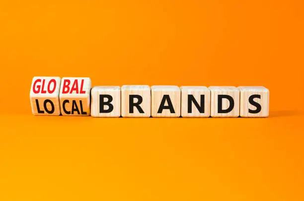 Photo of Global or local brands symbol. Concept words Global brands and Local brands on wooden cubes. Beautiful orange table orange background. Business global or local brand concept. Copy space.