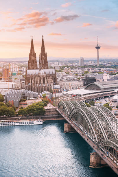 istock Cologne Aerial vertical view with trains move on a bridge over the Rhine River on which cargo barges and passenger ships ply. Majestic Cologne Cathedral in the background 1449866488