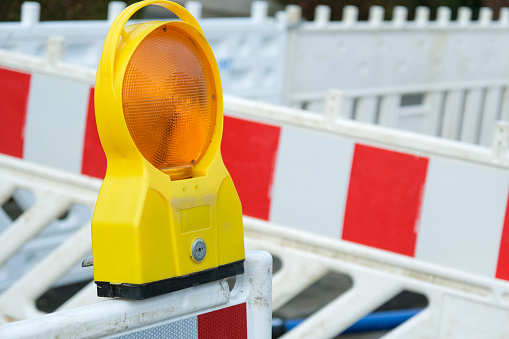 Construction site concept: Close-up of a construction site lamp on a red and white barrier in front of a secured excavation pit, selective focus, copy space
