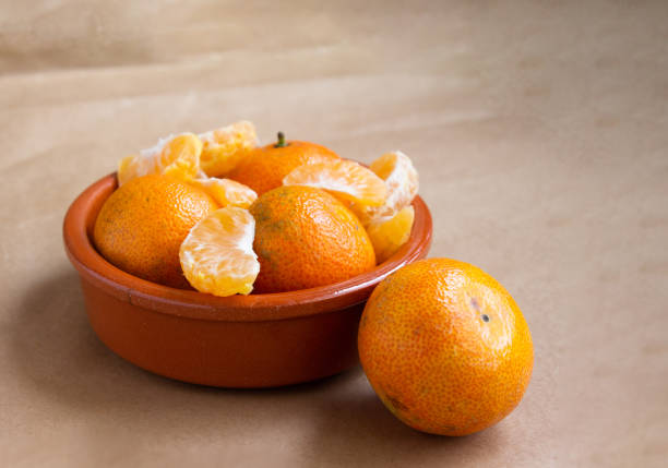 istock mandarin slices and whole fruit in a brown bowl on a light brown background 1449866766