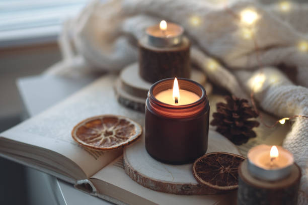 istock Cozy autumn or winter composition with aromatic candle, wool sweater, book. Aromatherapy, home atmosphere of cosiness and relax. Wooden background close up. 1449868903
