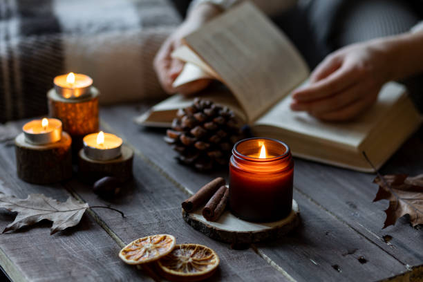 istock Cozy autumn or winter composition with aromatic candle, wool sweater, book. Aromatherapy, home atmosphere of cosiness and relax. Wooden background close up. Woman reading a book 1449868905