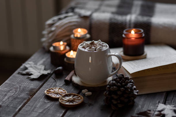 istock Autumn cozy home composition with hot chocolate with marshmallow and candles. Aromatherapy on a grey fall morning, atmosphere of cosiness and relax. Wooden background, books, close up. 1449868948