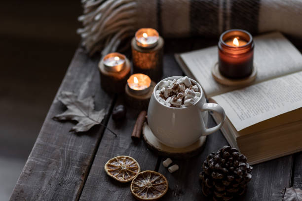 istock Autumn cozy home composition with hot chocolate with marshmallow and candles. Aromatherapy on a grey fall morning, atmosphere of cosiness and relax. Wooden background, books, close up. 1449868950