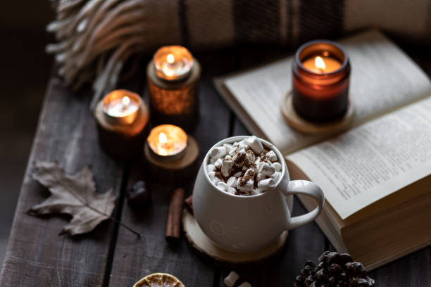 istock Autumn cozy home composition with hot chocolate with marshmallow and candles. Aromatherapy on a grey fall morning, atmosphere of cosiness and relax. Wooden background, books, close up. 1449868951