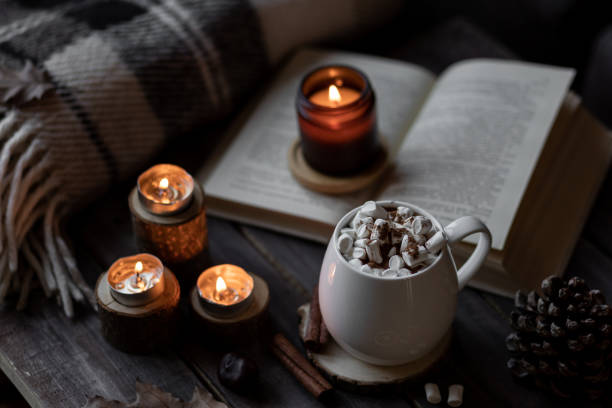 istock Autumn cozy home composition with hot chocolate with marshmallow and candles. Aromatherapy on a grey fall morning, atmosphere of cosiness and relax. Wooden background, books, close up. 1449868957