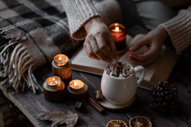istock Autumn cozy home composition with hot chocolate with marshmallow and candles. Aromatherapy on a grey fall morning, atmosphere of cosiness and relax. Wooden background, books, close up. 1449868963