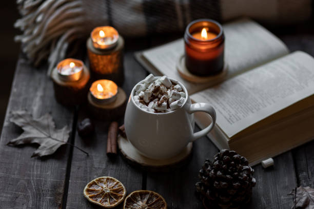 istock Autumn cozy home composition with hot chocolate with marshmallow and candles. Aromatherapy on a grey fall morning, atmosphere of cosiness and relax. Wooden background, books, close up. 1449868973