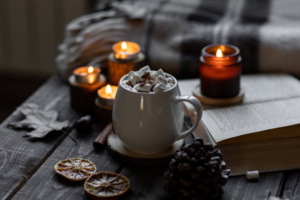 istock Autumn cozy home composition with hot chocolate with marshmallow and candles. Aromatherapy on a grey fall morning, atmosphere of cosiness and relax. Wooden background, books, close up. 1449868975