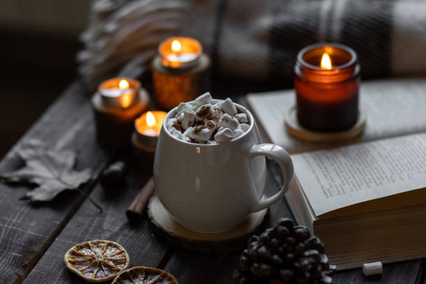 istock Autumn cozy home composition with hot chocolate with marshmallow and candles. Aromatherapy on a grey fall morning, atmosphere of cosiness and relax. Wooden background, books, close up. 1449868977