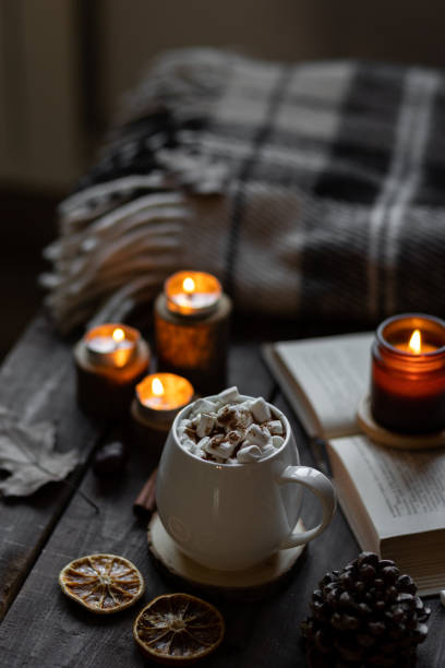 istock Autumn cozy home composition with hot chocolate with marshmallow and candles. Aromatherapy on a grey fall morning, atmosphere of cosiness and relax. Wooden background, books, close up. 1449868990