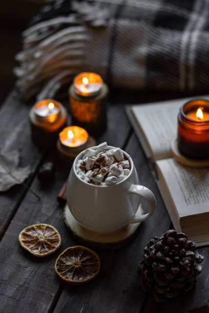 istock Autumn cozy home composition with hot chocolate with marshmallow and candles. Aromatherapy on a grey fall morning, atmosphere of cosiness and relax. Wooden background, books, close up. 1449868992