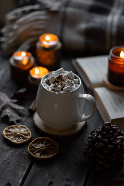 istock Autumn cozy home composition with hot chocolate with marshmallow and candles. Aromatherapy on a grey fall morning, atmosphere of cosiness and relax. Wooden background, books, close up. 1449868998