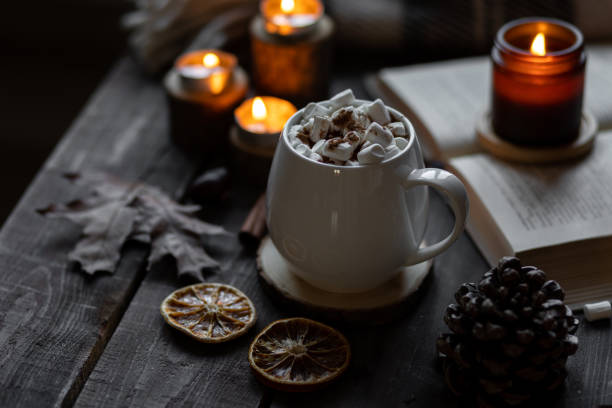 istock Autumn cozy home composition with hot chocolate with marshmallow and candles. Aromatherapy on a grey fall morning, atmosphere of cosiness and relax. Wooden background, books, close up. 1449869004