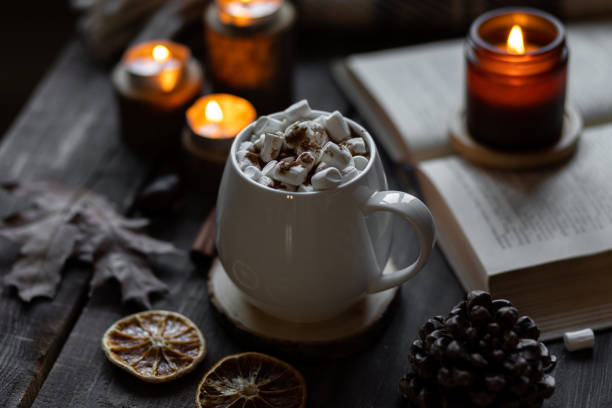 istock Autumn cozy home composition with hot chocolate with marshmallow and candles. Aromatherapy on a grey fall morning, atmosphere of cosiness and relax. Wooden background, books, close up. 1449869005