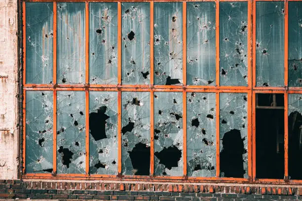 Photo of Building in industrial zone with windows broken from stones, bullets and shards. The concept of military conflict, ghettos and social theory of broken glass