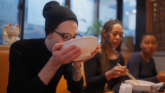 A group of multi-racial group of friends tourists are enjoying experiencing and having Japanese food ramen in a ramen shop during their travel.