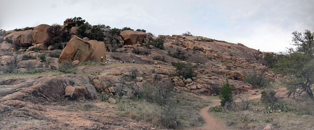 A panaromic view taken at Enchanted rock state park in Texas usa. A reddish colored rocky landscape is presented