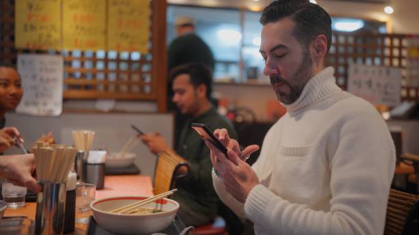male tourist taking photos of ramen with his smart phone. group of multi-racial group of friends tourists enjoying experiencing and having japanese food ramen in ramen shop - japanese culture japan japanese ethnicity asian and indian ethnicities imagens e fotografias de stock