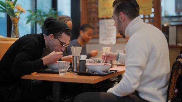 group of multi-racial group of friends tourists enjoying experiencing and having japanese food ramen in ramen shop - japanese culture japan japanese ethnicity asian and indian ethnicities imagens e fotografias de stock