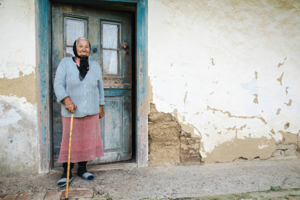 Grandmother standing beside her house with a cane