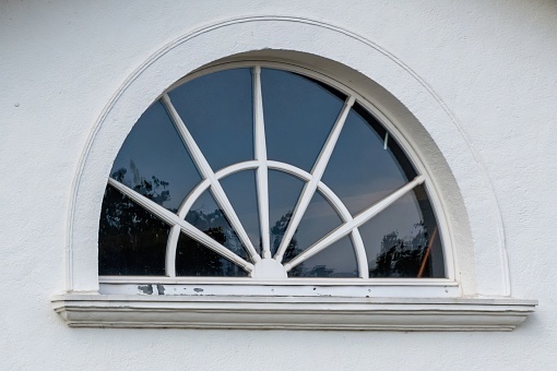 A closeup of a semi circular window with sunburst design on a white wall of a house