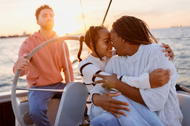 Family Yacht Sailing in the sunset Father sailing the yacht while mother and daughter embrace and enjoy the view. Luxury vacation at sea. boating stock pictures, royalty-free photos & images