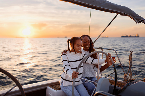 Teenage girl steers a yacht while sailing with her mother.  Luxury vacation at sea.