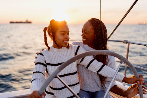 Teenage girl steers a yacht while sailing with her mother.  Luxury vacation at sea.