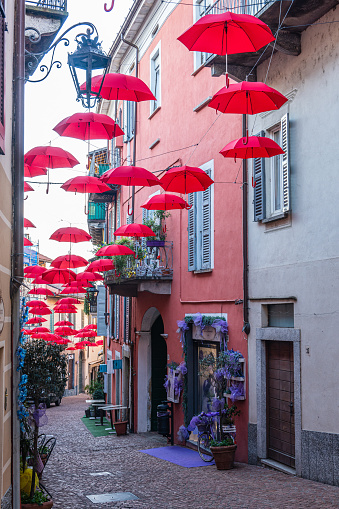 luino, Italy - 12-06-2022: Beautiful street in the historic center with colorful shops and hanging red umbrellas in Luino