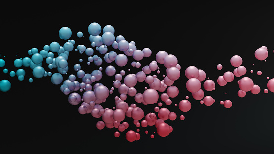 Smaller and larger spheres flow in space while changing colour from left to right in a wavy motion. 3D digital render