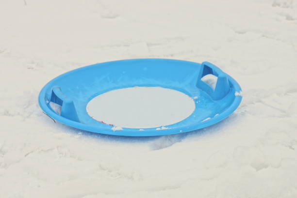 one round blue plastic sled plate lies on a snowdrift of white snow in the street