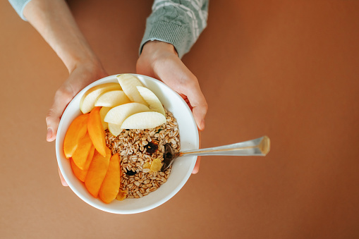 Close up of bowl with fresh oatmeal and spoon in woman hands, healthy and nutritive breakfast concept. Unrecognizable lady holding delicious homemade granola, breakfast at home. Top view. Copy space