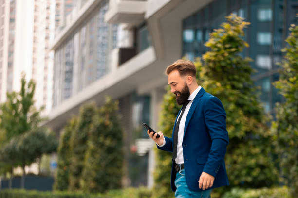 istock Smiling Caucasian businessman using smartphone while walking outdoors. 1449927085