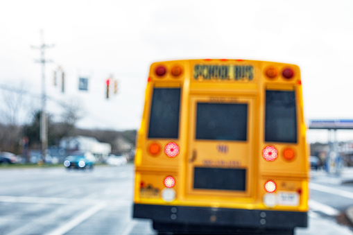 Car driver point of view of an abstract defocused school bus waiting ahead at traffic light road intersection.